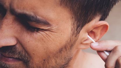 Man trying to clean his ears with a cotton bud