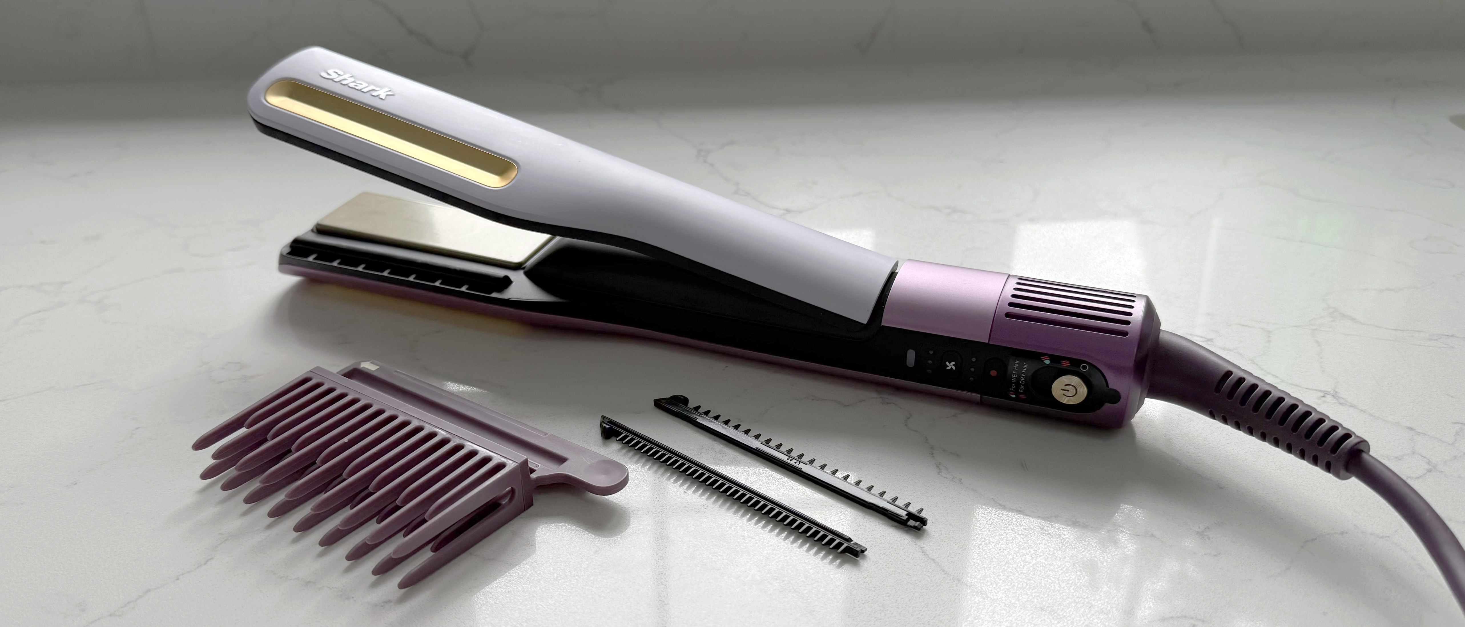 Shark SilkiPro Straight Plum Satin styler with wide-tooth, gentle, and precision comb attachments displayed beside it on a marble surface