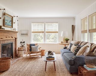 Long white living room with neutral color palette, large jute rug, blue sofa and wood-framed fireplace.