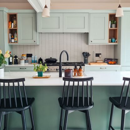 Green kitchen cabinets with black bar stools around kitchen island