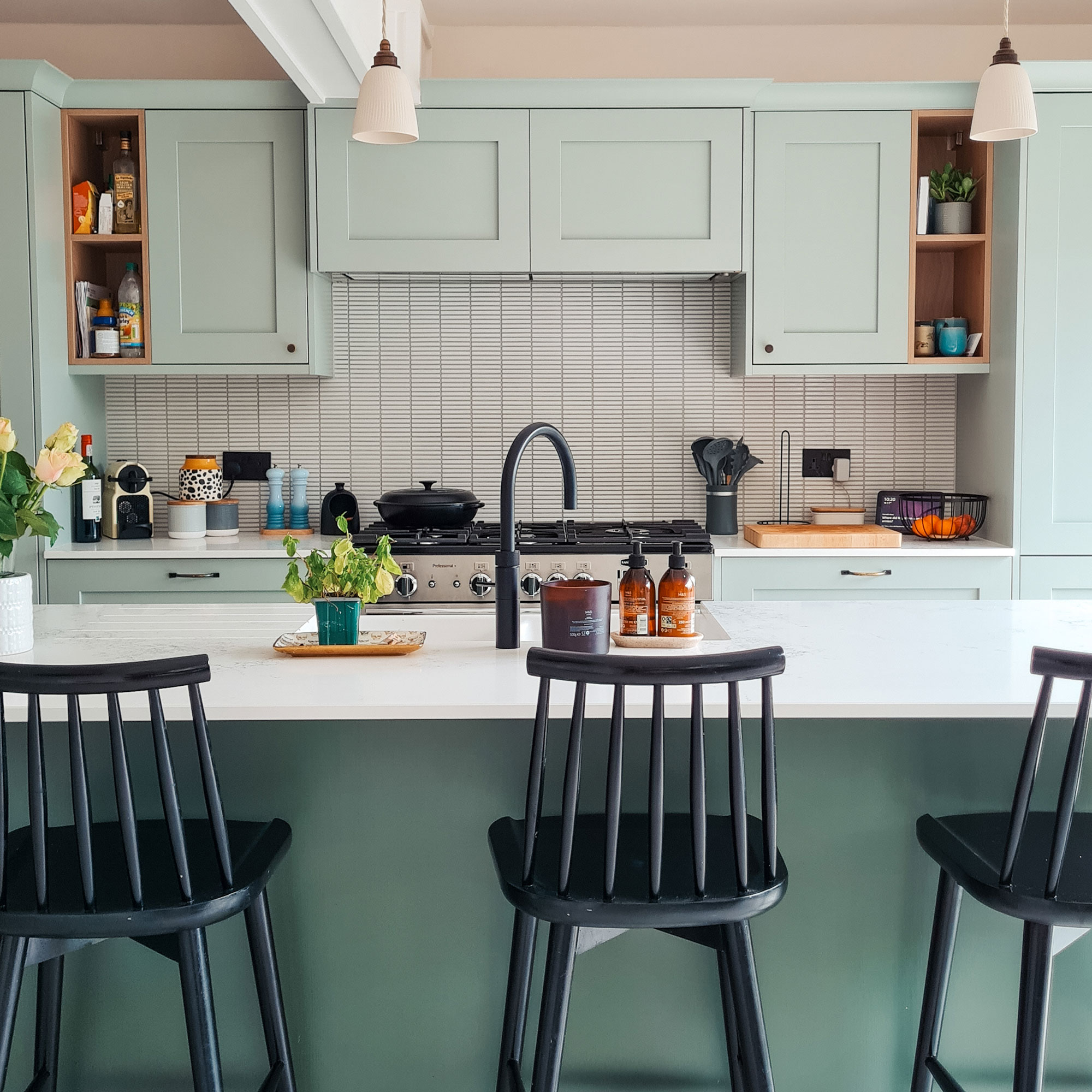 Green kitchen cabinets with black bar stools around kitchen island