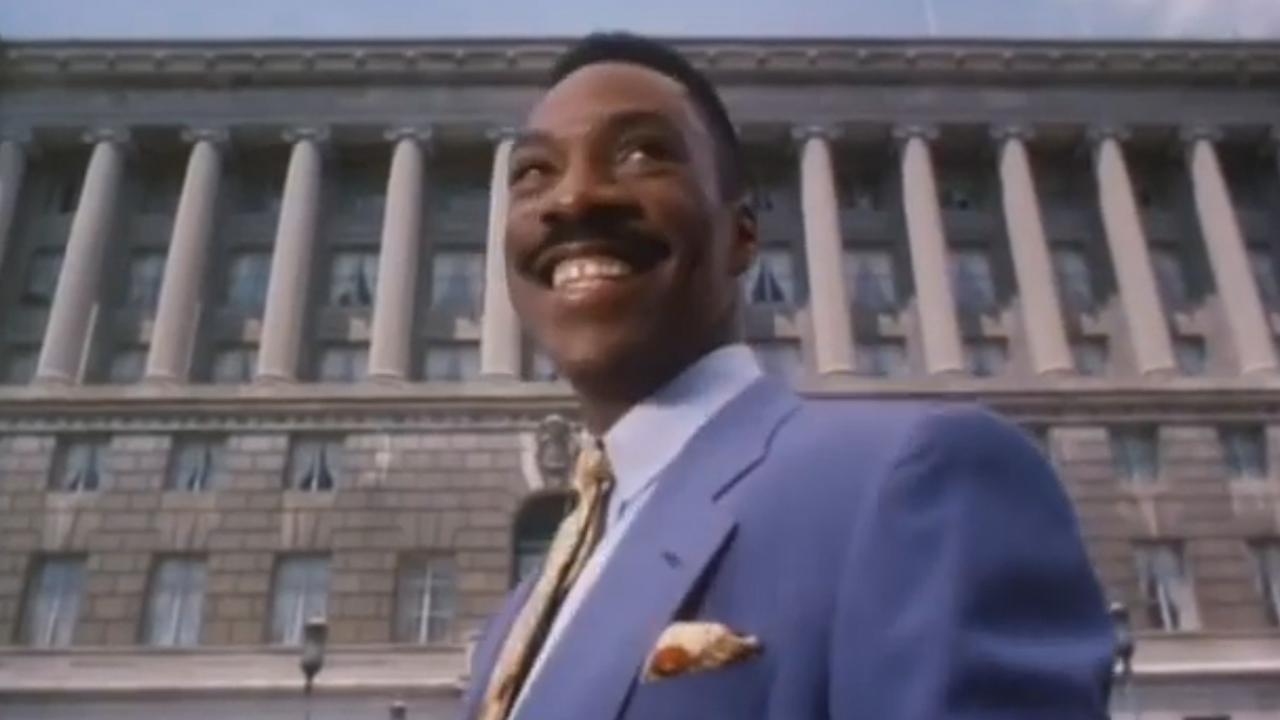 Eddie Murphy wearing a suit and smiling in front of a government building in The Distinguished Gentleman