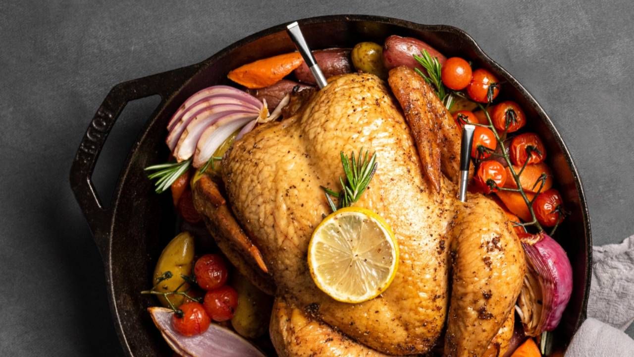 A roast chicken sat on vegetables with two meat thermometers inside it