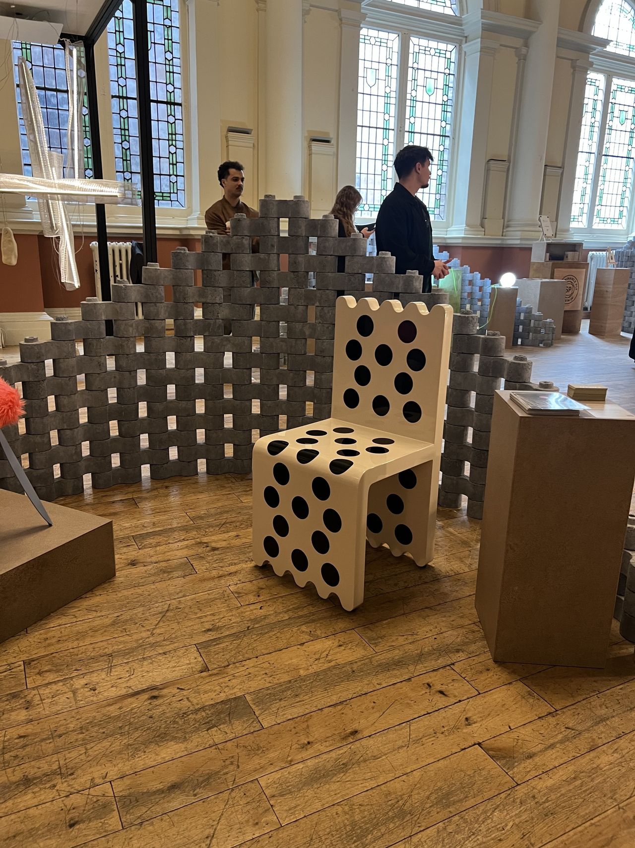 Image of a gallery showroom with a display including a black and white polka dot chair and a divider wall made out of concrete bricks.