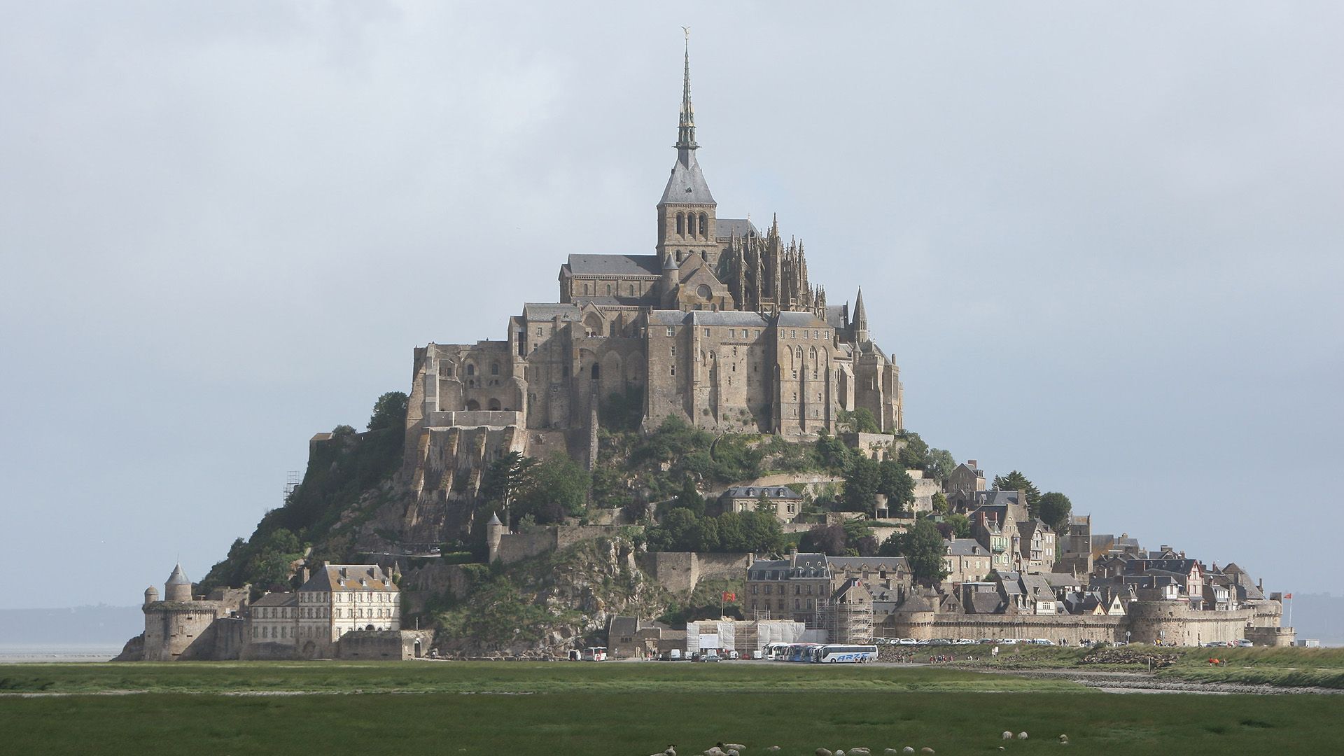 A view of a tall brown castle with spires and walls around it on the top of a hill.