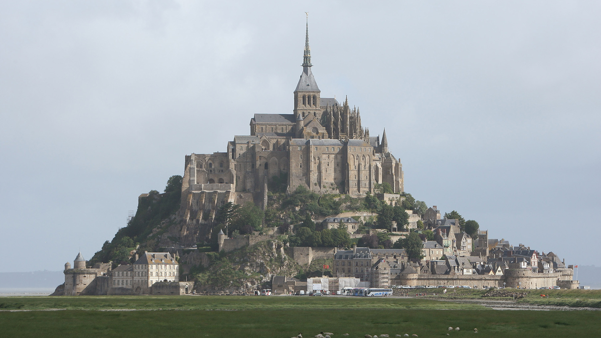 A view of a tall brown castle with spires and walls around it on the top of a hill.