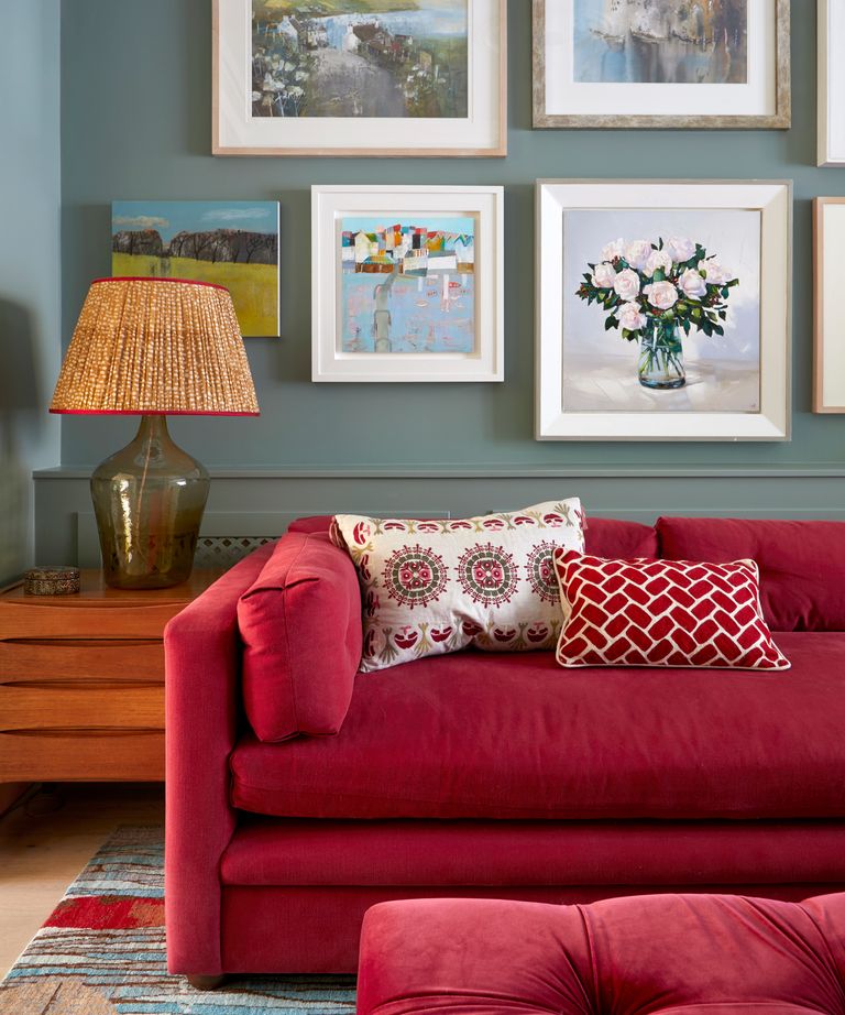 A red sofa and cushions in a traditional living room with vintage artwork