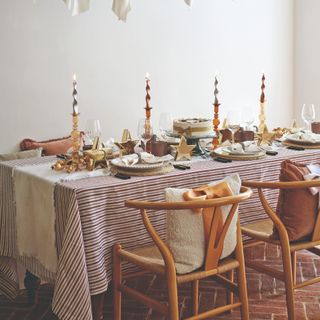 A dining table set for a Christmas dinner with the cushions on the dining wishbone chairs decorated with bows