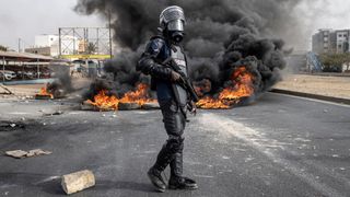 A Senegalese gendarme standing near burning tyres