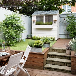 Small garden with patio and small lawn with a cream shed at the bottom of the garden