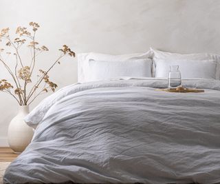 A magnolia bed with linen sheets on with a large vase beside it