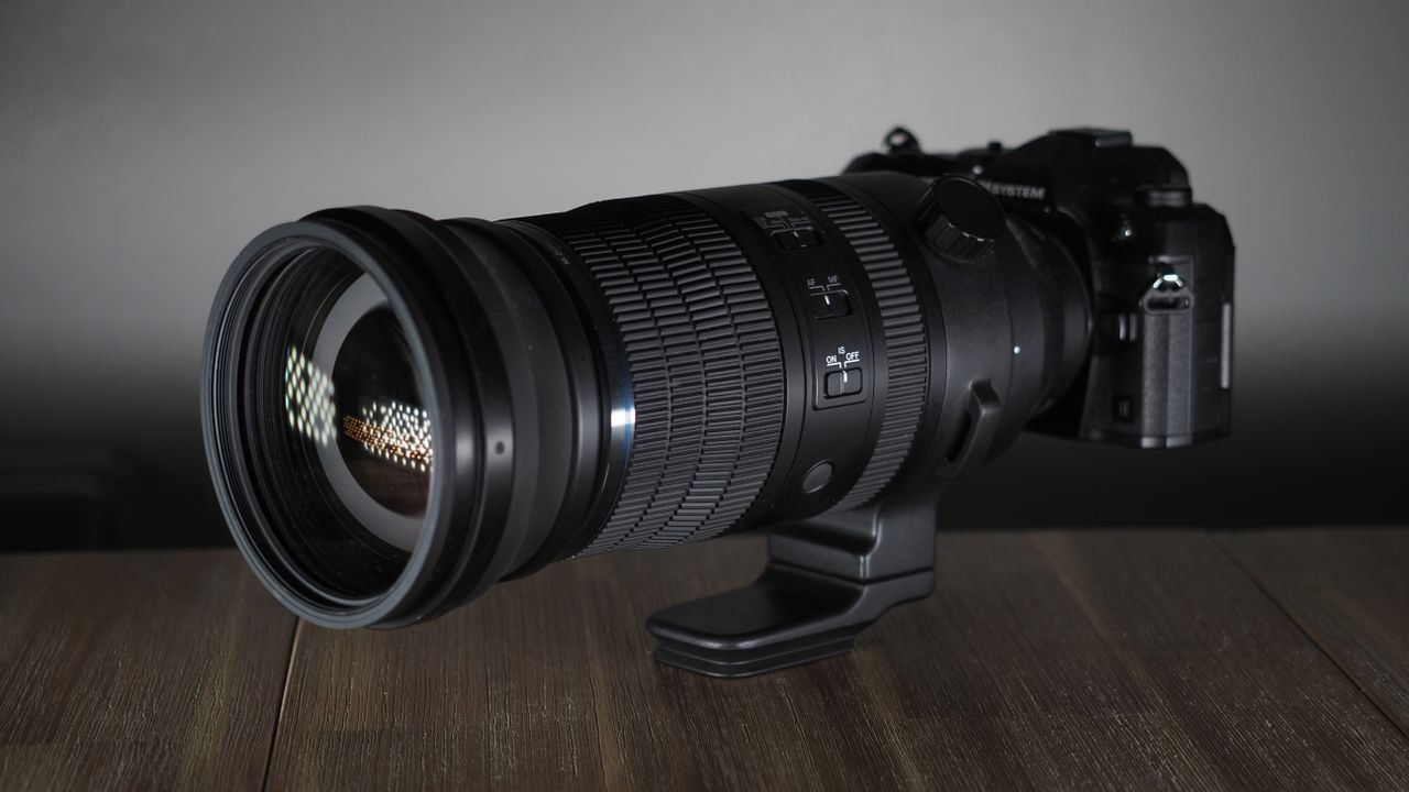 OM System M.Zuiko 150-600mm f/5.0-6.3 IS lens, mounted to an OM System OM-1 Mark II, on a wooden surface lit with moody lighting