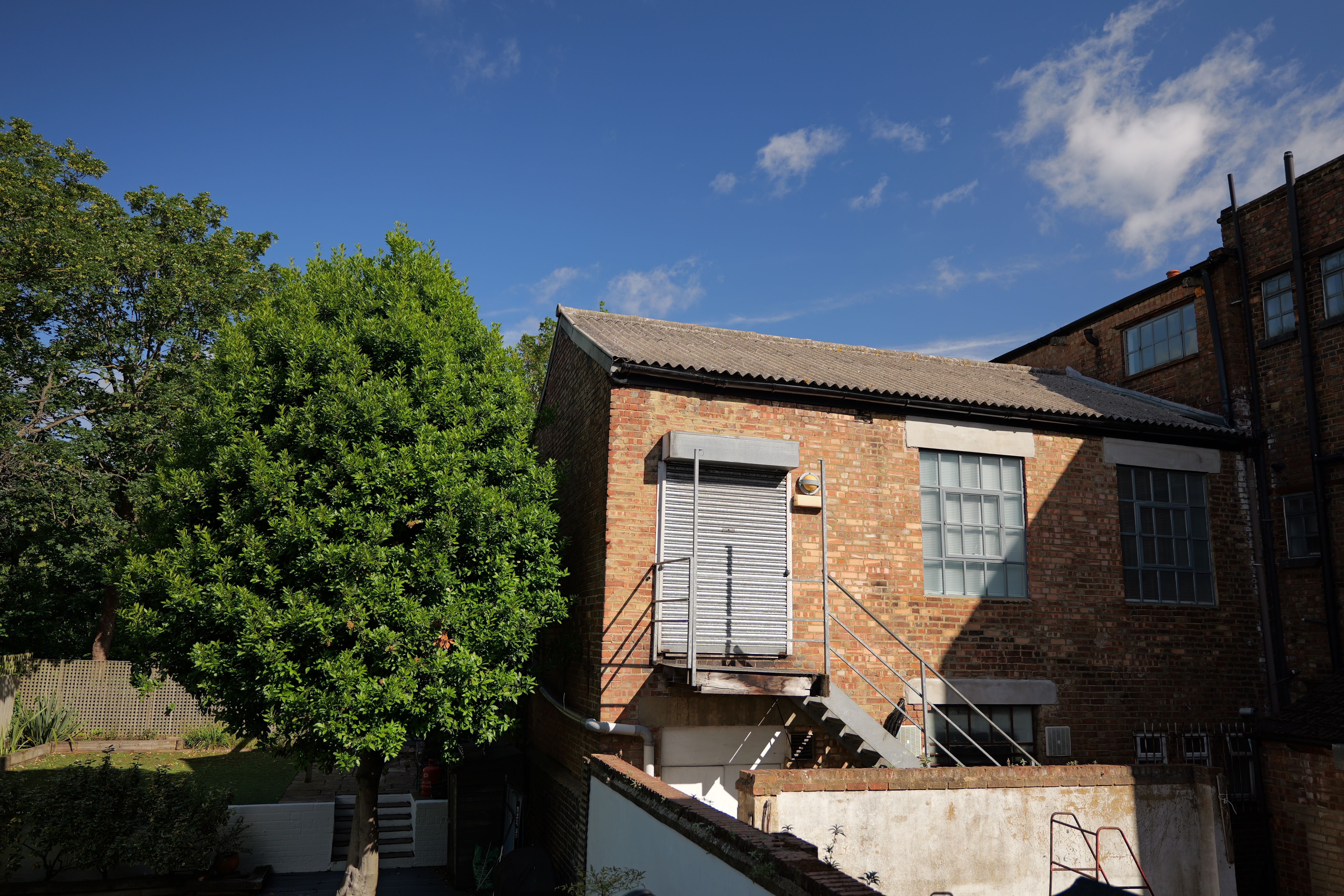 A warehouse next to a tree in front of a bright blue sky