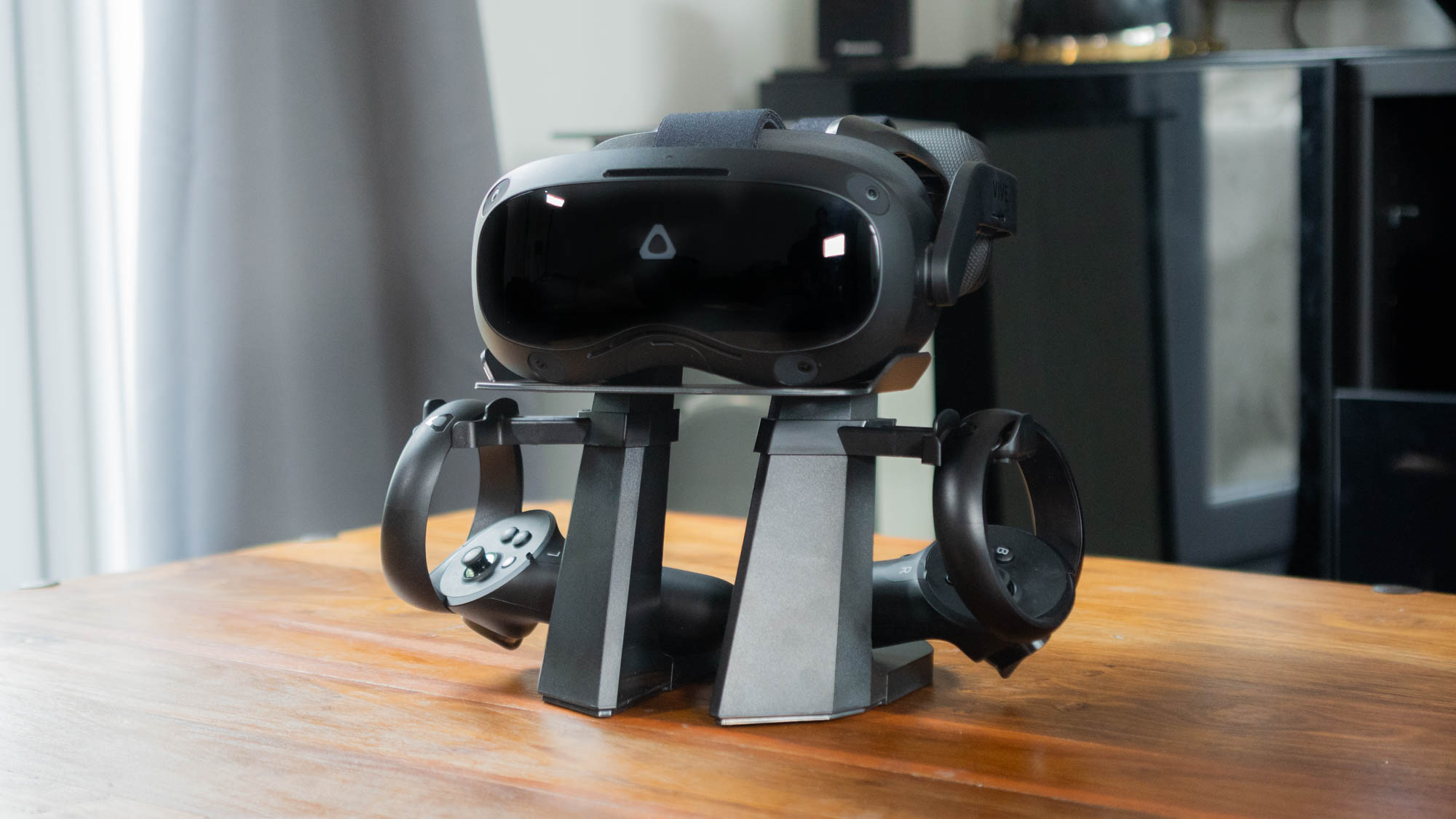 A photograph of the HTC Vive Focus 3 and its controllers, mounted on a stand on a coffee table