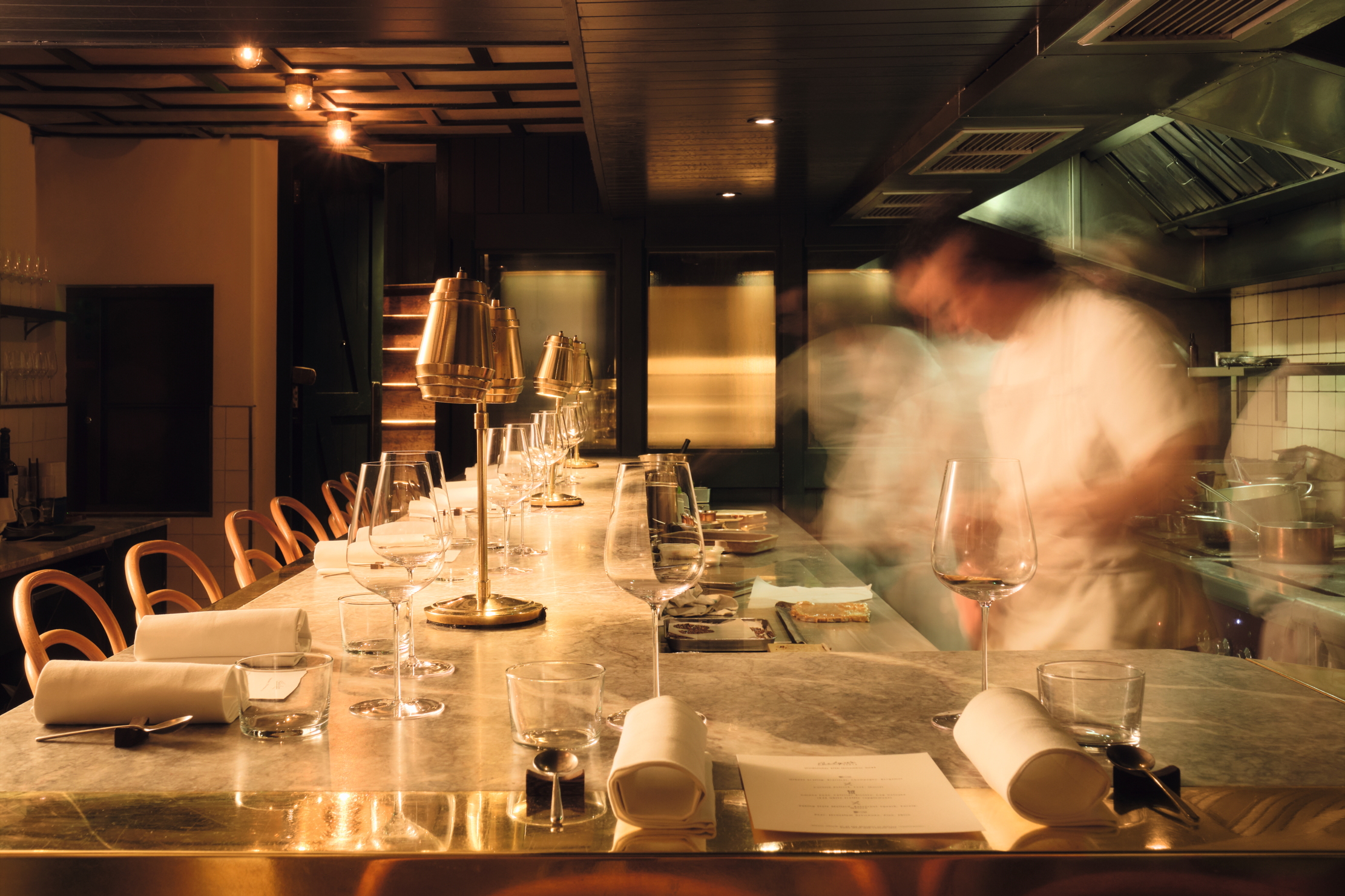 A long exposure of the Chef's Table at Evelyn's Table, where the foreground is in focus but chefs whiz around blurrily
