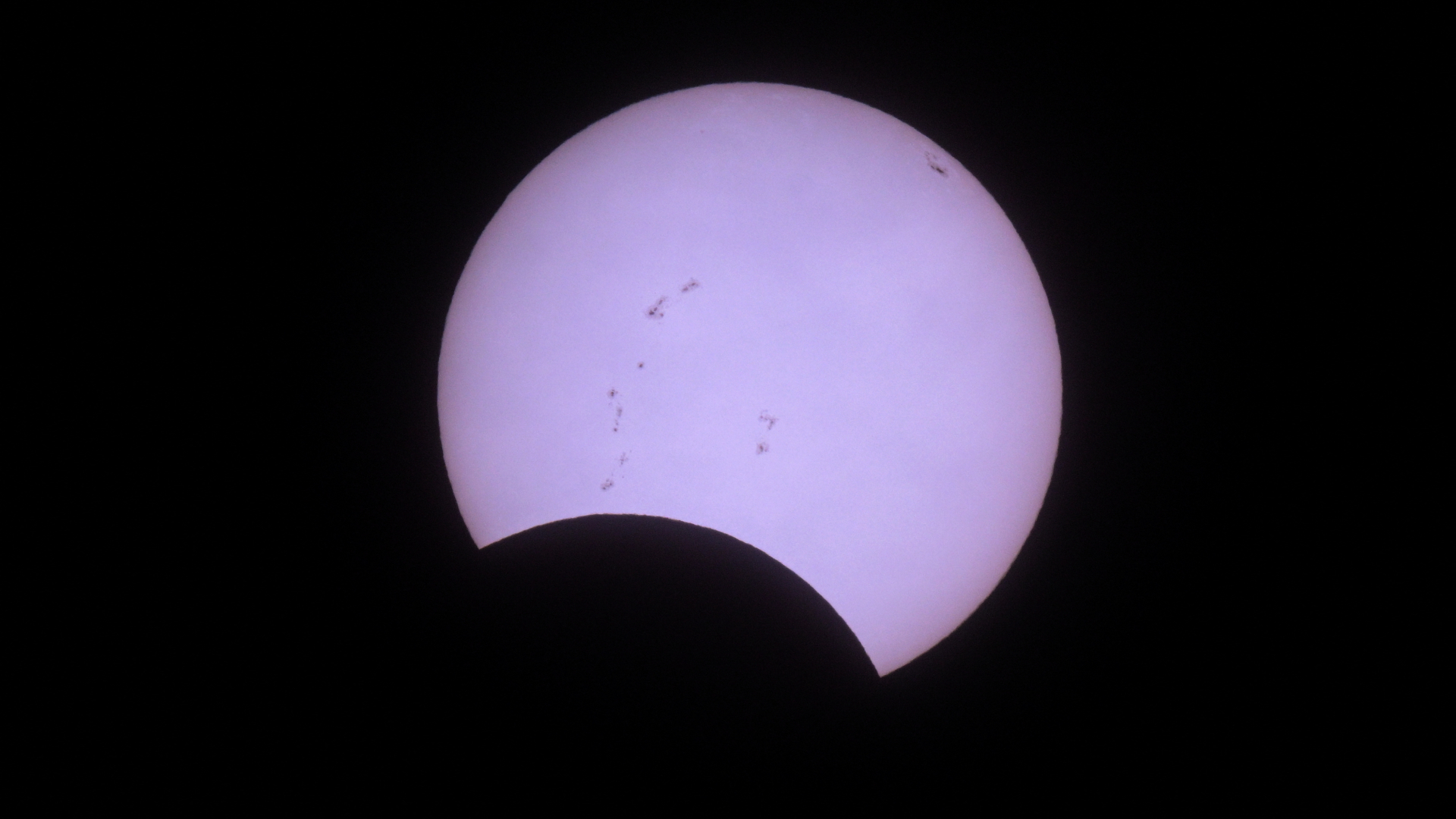 The sun's disk is pictured against a black sky with its lower section obscured by the moon's silhouette during an eclipse.