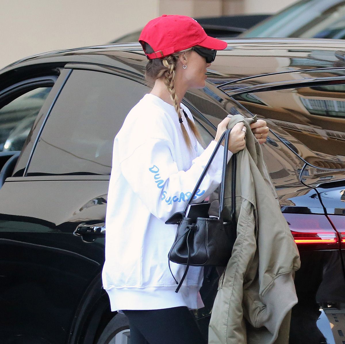 Margot Robbie in L.A. wearing a red baseball cap, white sweatshirt, black leggings, and Loewe Flow Runner sneakers