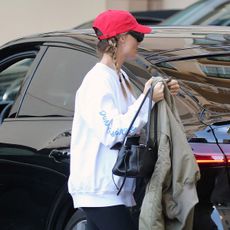 Margot Robbie in L.A. wearing a red baseball cap, white sweatshirt, black leggings, and Loewe Flow Runner sneakers