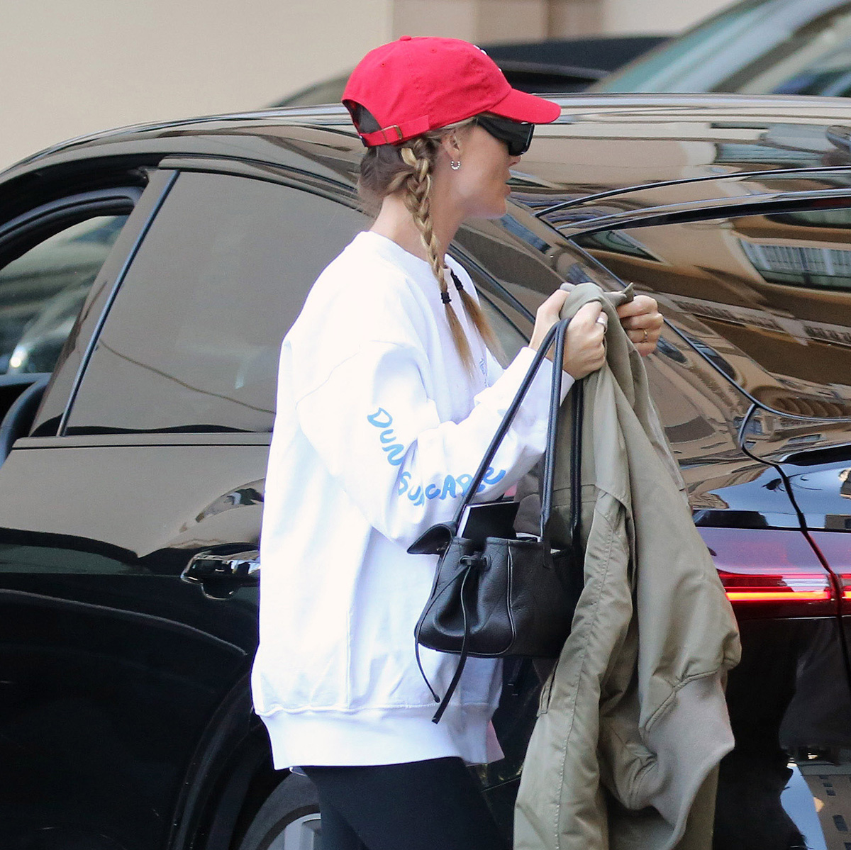 Margot Robbie in L.A. wearing a red baseball cap, white sweatshirt, black leggings, and Loewe Flow Runner sneakers