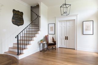Neutral toned entryway with a modern chandelier and various antique style pieces