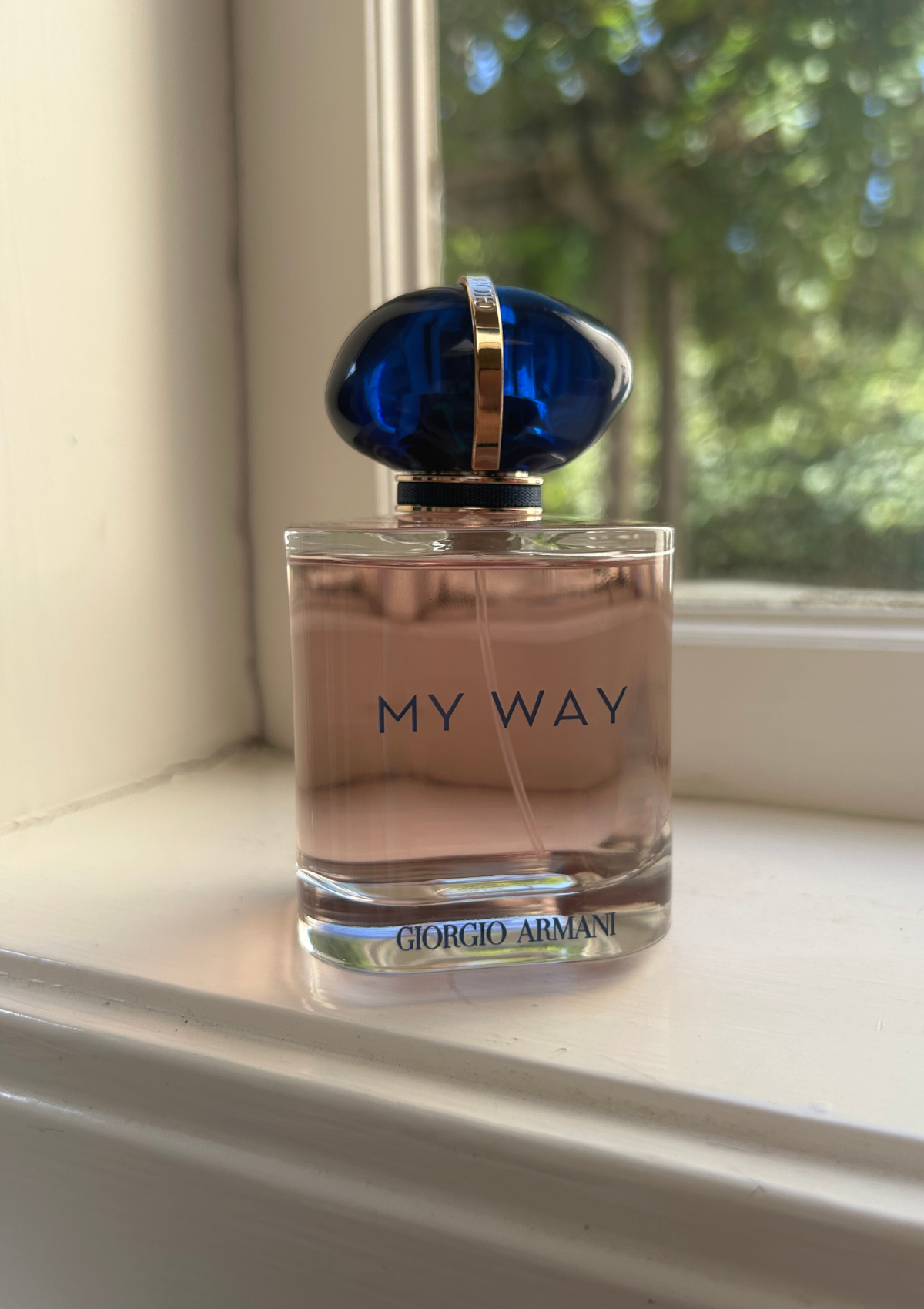 My Way by Giorgio Armani sitting on a sunny windowsill, blue cap catching the light with trees blurred in the background.