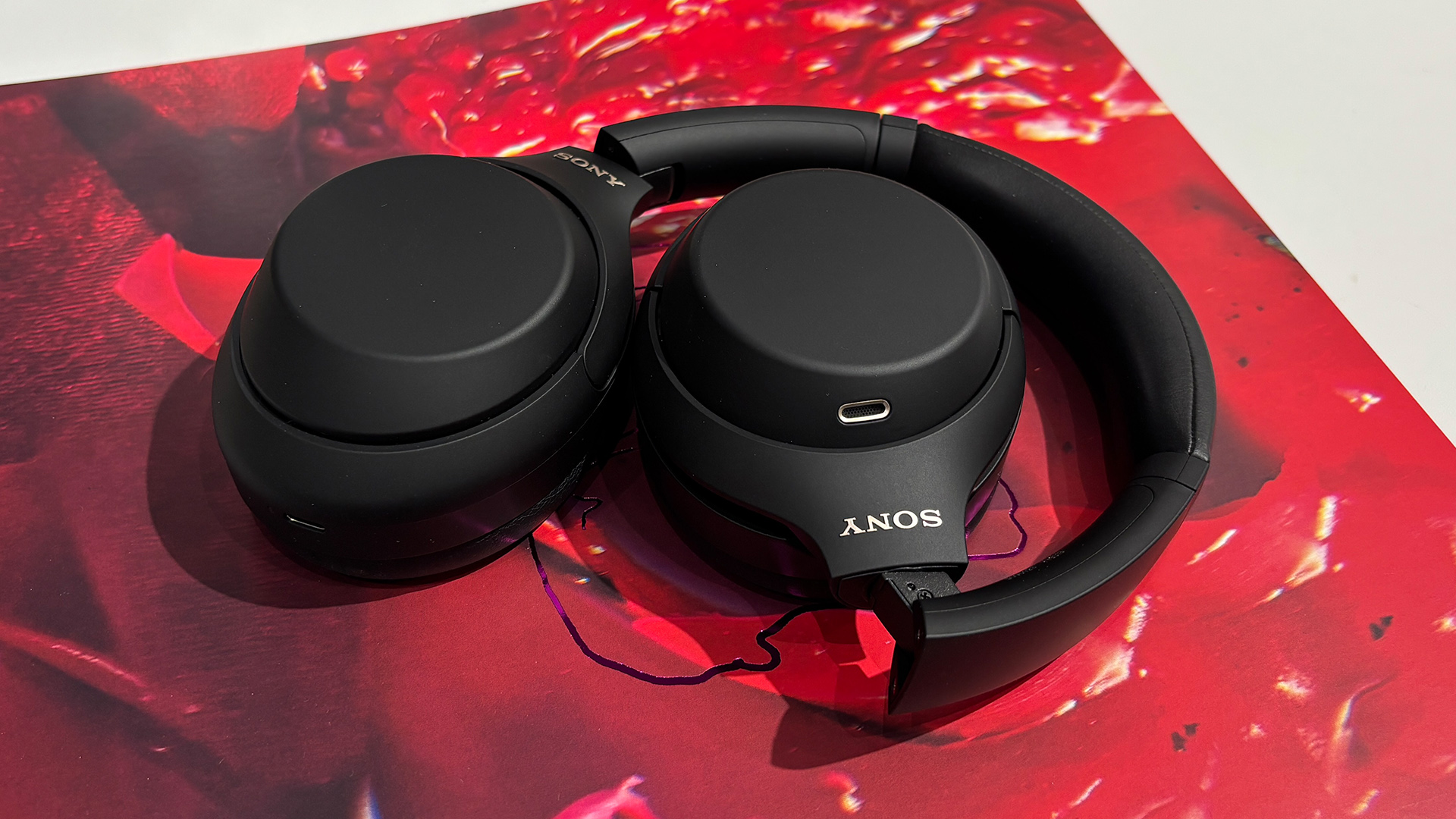 Sony WH-1000XM4C over-ear headphones lying flat, ear cup down on red LP