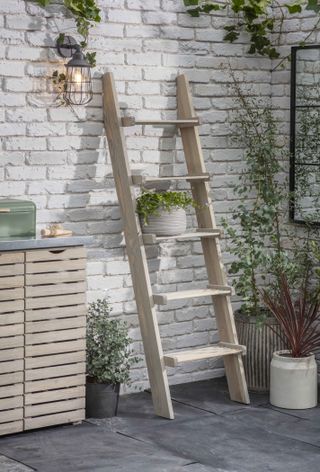 An outdoor pendant wall light on a white brick wall next to a wooden plant shelf