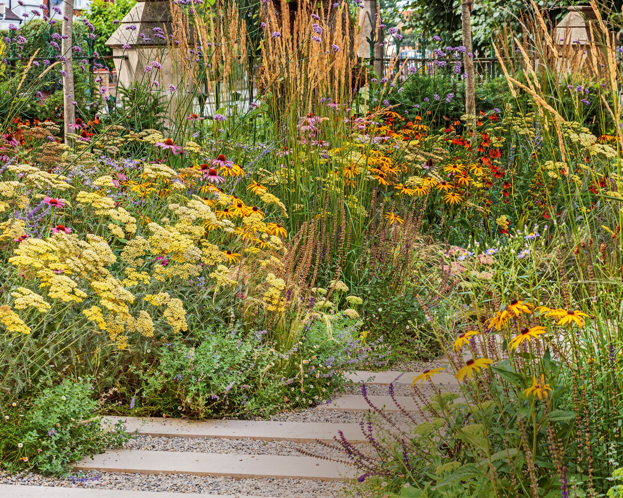 Wild flowers lining a brick path, lots of greenery and trees in background