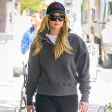 Jennifer Lawrence wears a gray sweatshirt, black La Ligne pants, red mesh mules, and black sunglasses.