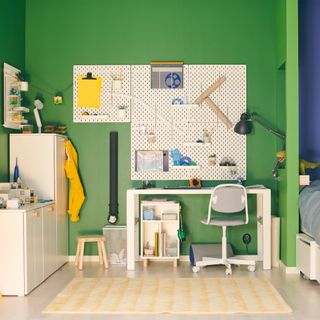 A white desk and pin board in a green kids bedroom