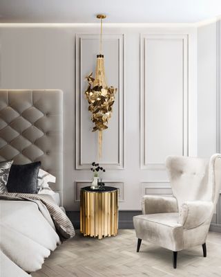Glamorous grey, gold and white bedroom by Luxxu, button backed headboard, herringbone floor, panelled walls, velvet armchair, gold bedside and intricate pendant light