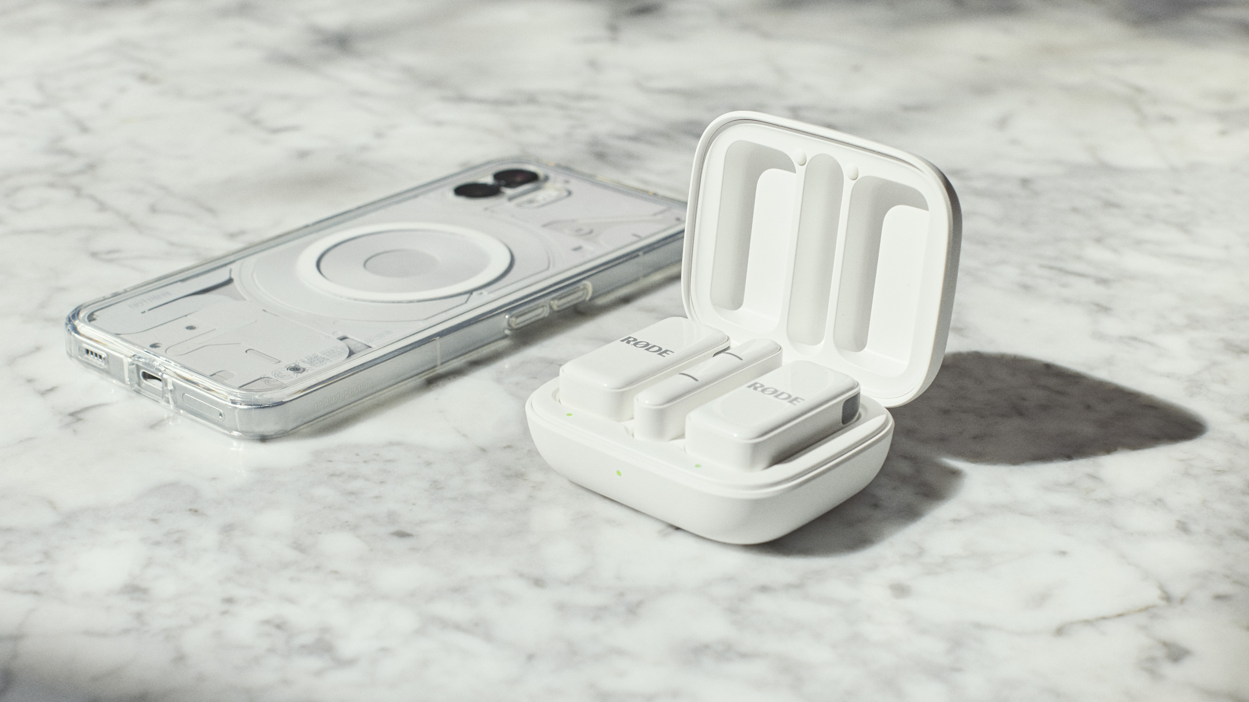 Rode Wireless Micro kit in charging case, alongside a smartphone on a marble surface