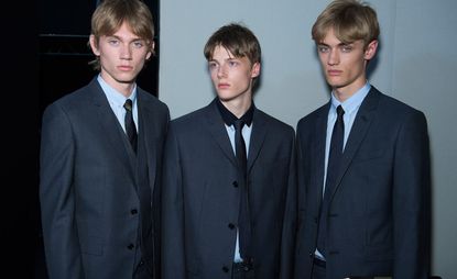Three male models wearing suites by Dior Homme in dark grey.