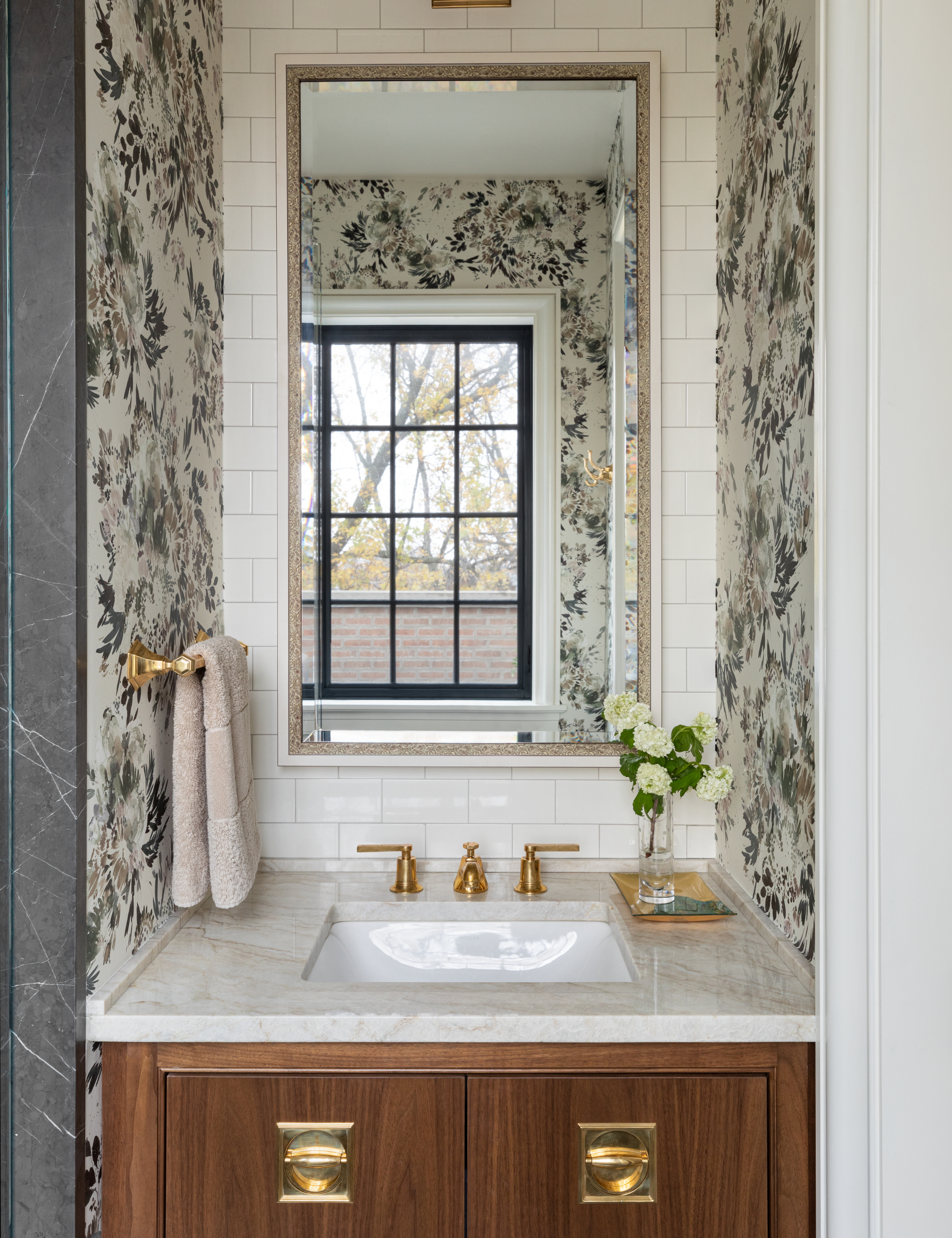Guest bathroom featuring patterned wallpaper, a nautral wood vanity, and a plush hand towel hanging from a brass towel rack