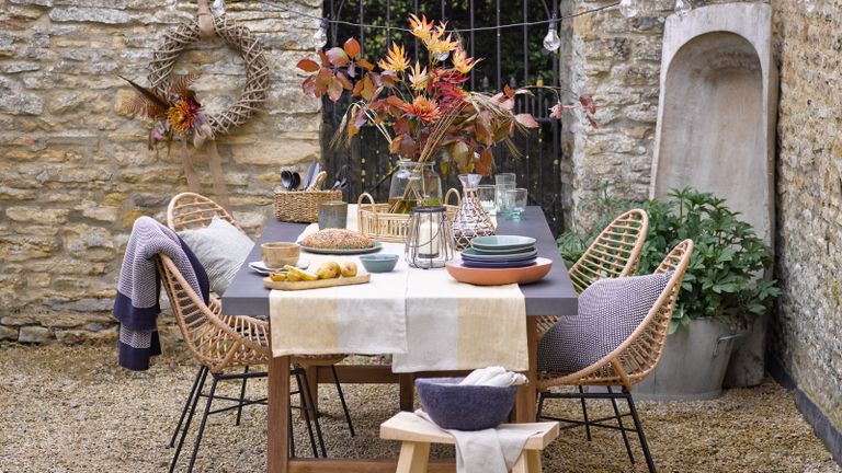 a dining table in an enclosed stone courtyard with fall and autumnal decor - Garden Trading