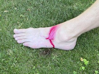 En fot med rödfärg mot en gräsmatta.