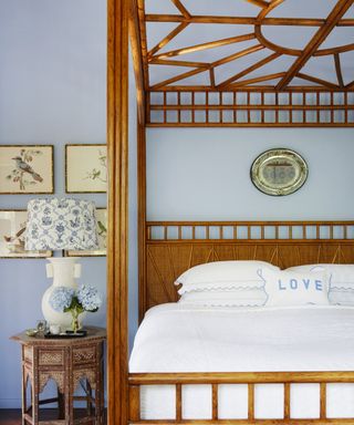 A periwinkle blue bedroom with wooden four poster bed, Moroccan-style bedside table and a gallery wall of traditional bird prints.