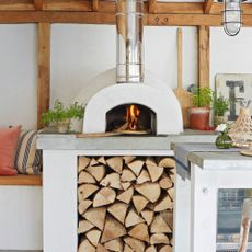 outdoor pizza oven with log pile next to bench seating