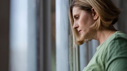 Close up side view of a sad woman as she looks out of a window