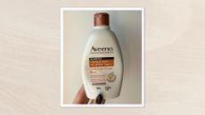 Hand holding the Aveeno Apple Cider Vinegar Shampoo bottle on a cream background