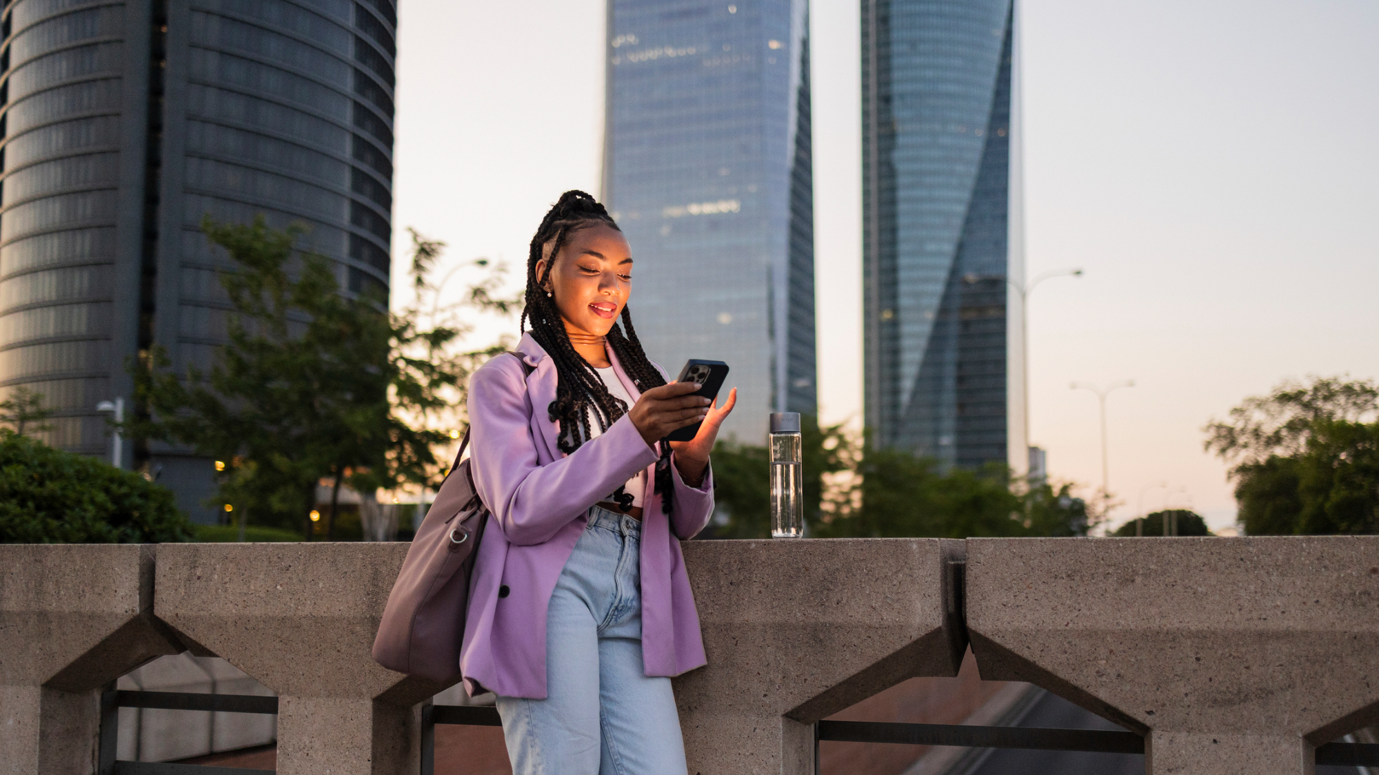 A person on their phone, walking past several high-rise buildings.