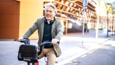 A mature man in glasses rides an e-bike down a city street.