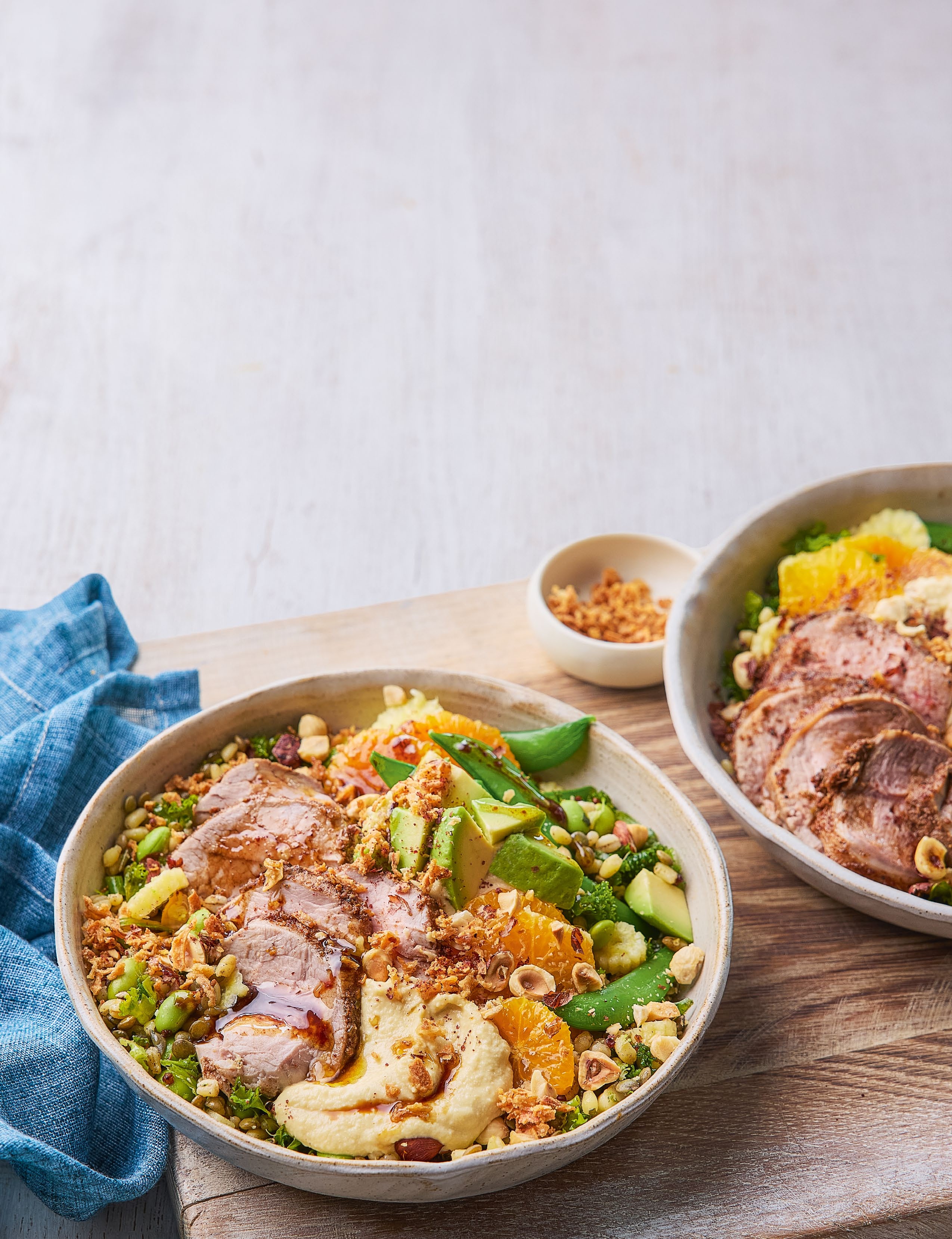 A vibrant bowl of grains and greens topped with tender grilled spiced pork, garnished with crunchy toppings, featured in a &#039;Meals that GIVE BACK&#039; article.