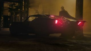 The Batman standing next to the Batmobile