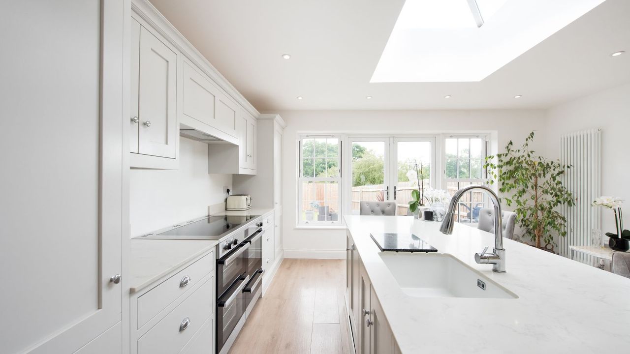 An all white minimalist kitchen with an island and light wood floors