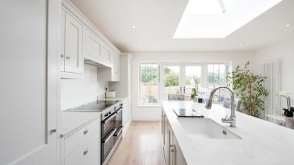 An all white minimalist kitchen with an island and light wood floors