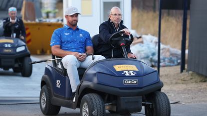 Bryson DeChambeau and a rules official drive in a golf cart