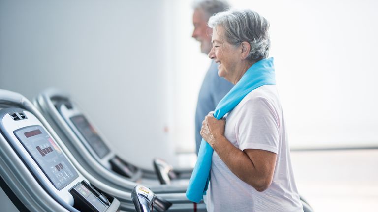 Elderly man and woman both are walking on treadmills