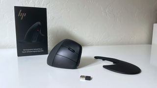 The HP 925 ergonomic vertical mouse on a white desk next to its box, detached palm rest, and USB dongle