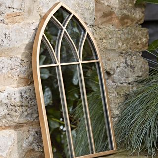 small gold arched mirror leaning up against a stone wall